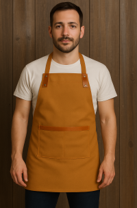 Delantal de cocina color habano en gabardina con aplicaciones de cuero café, diseño ajustable con bolsillo frontal, ideal para uso profesional en Chile